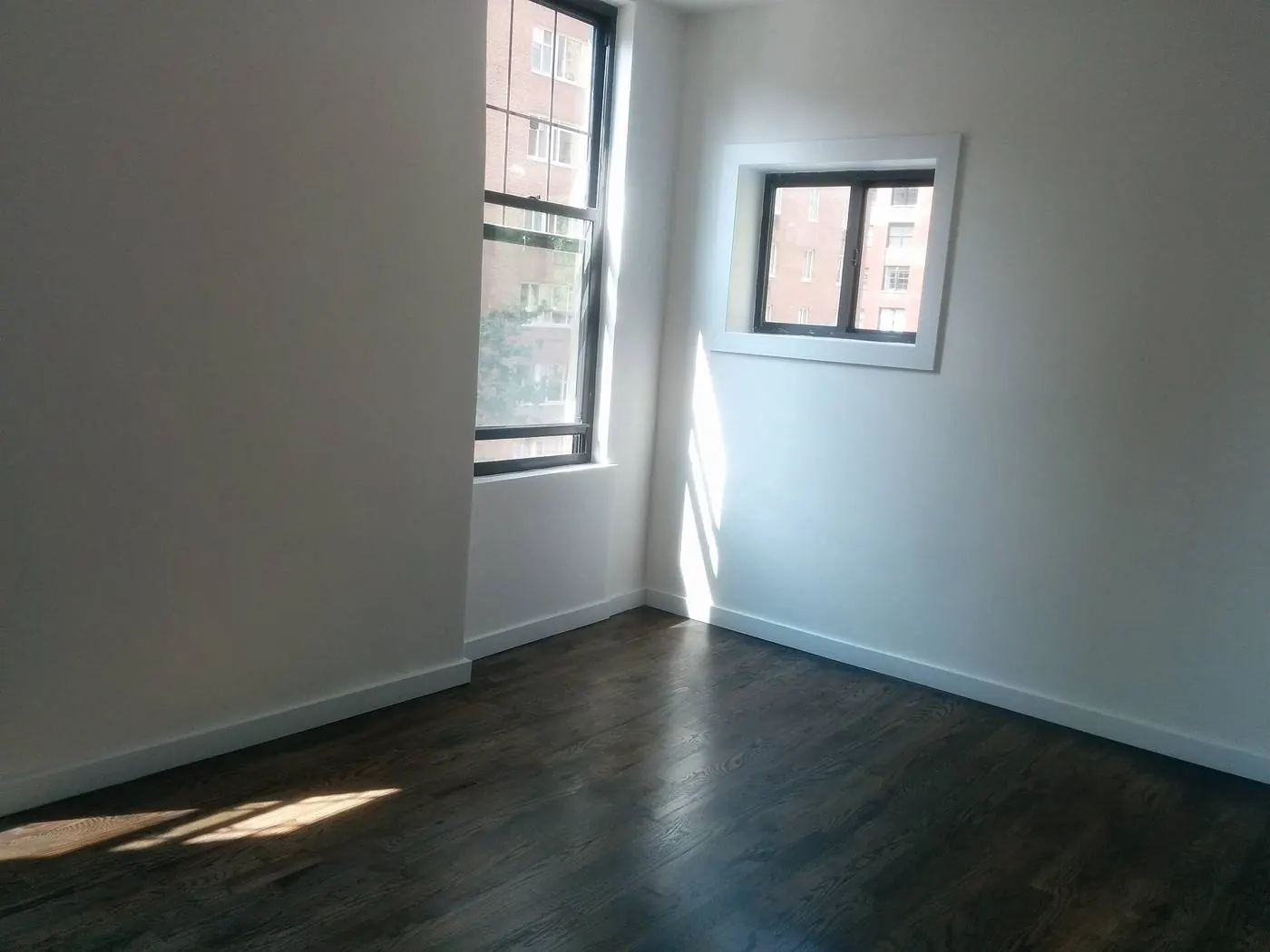 Pièce vide baignée de soleil, deux fenêtres d'angle, parquet sombre