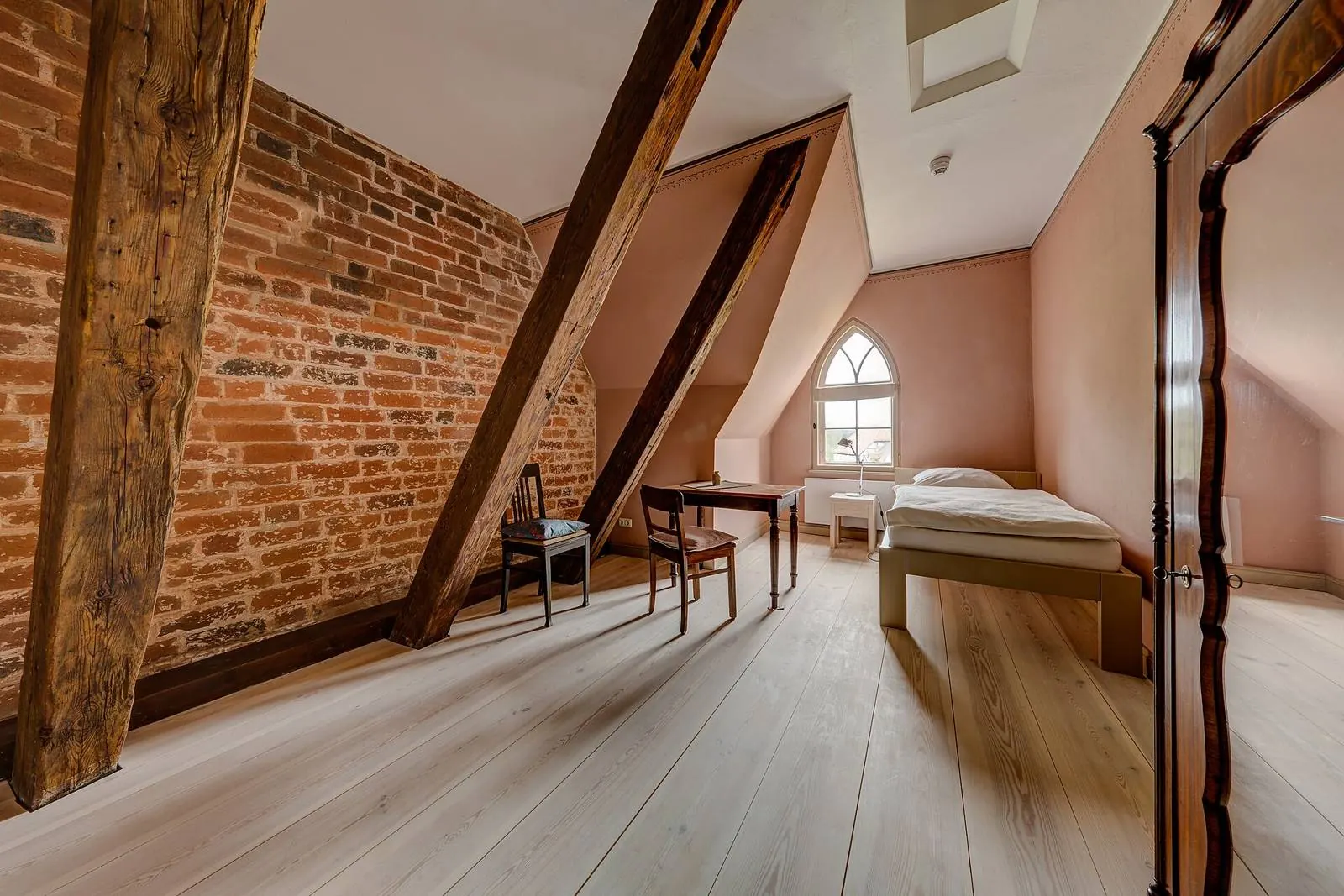 Chambre sous combles, charpente apparente, mur de brique et parquet clair