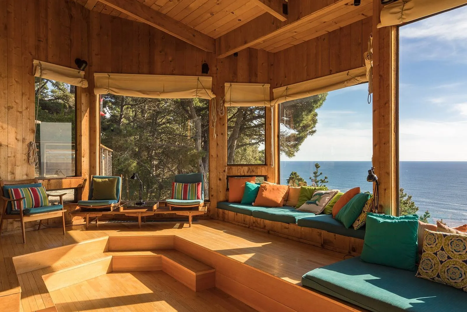 Salon en bois clair avec banquette sous une grande baie ouverte sur l'océan